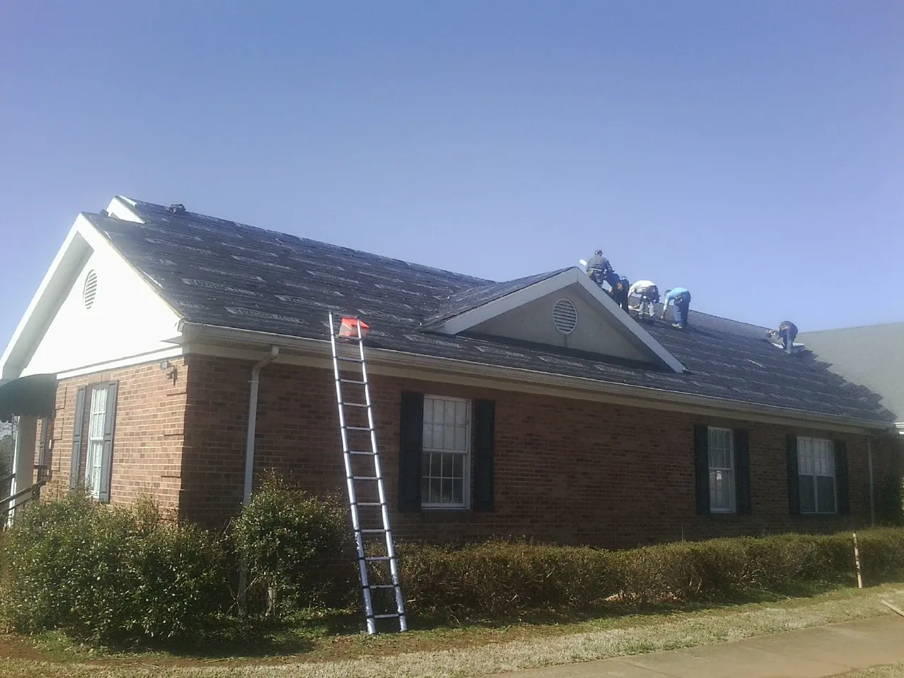 Crew tearing shingles off a brick ranch roof with a ladder set — Emergency Roof Repair work by our crew in Thiells