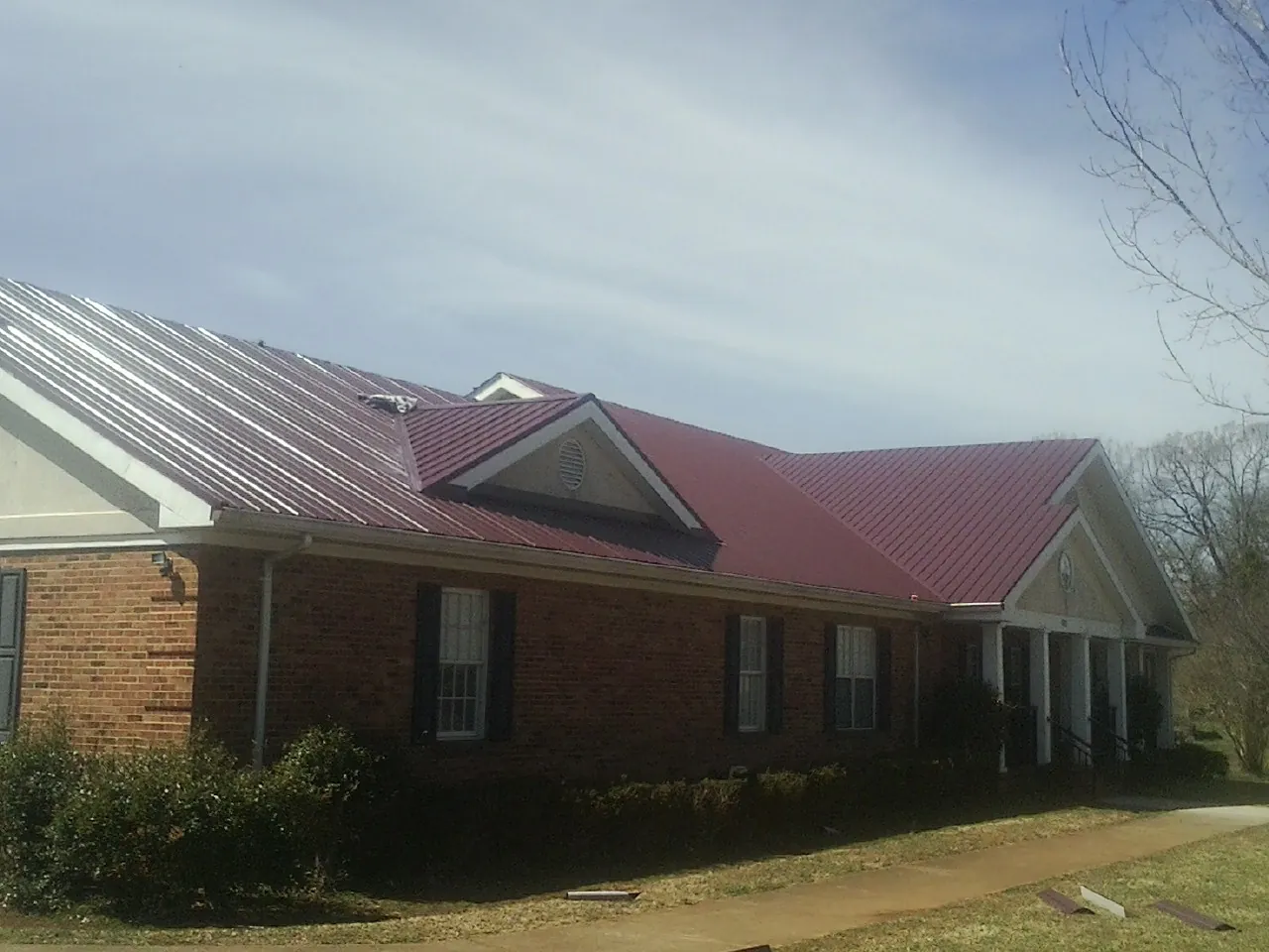 Red metal roof with gabled entries on a long brick building, from a Hail Damage Roof Repair job in Thiells