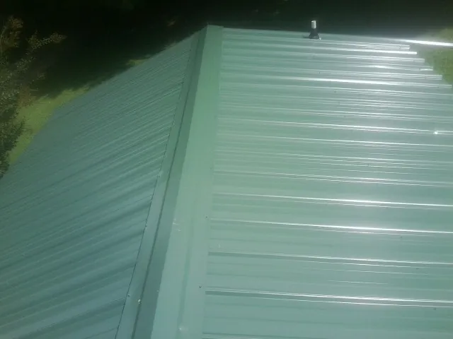 New green metal panels meeting at the ridge of a roof — Flat Roof Repair work by our crew in Thiells