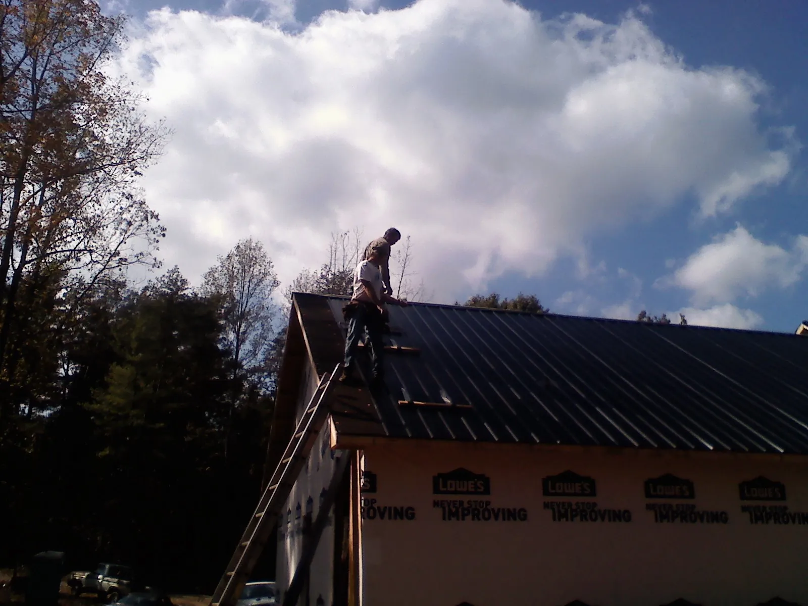 Roofer fastening dark metal panels high against a cloudy sky, from a Roof Inspection job in Thiells