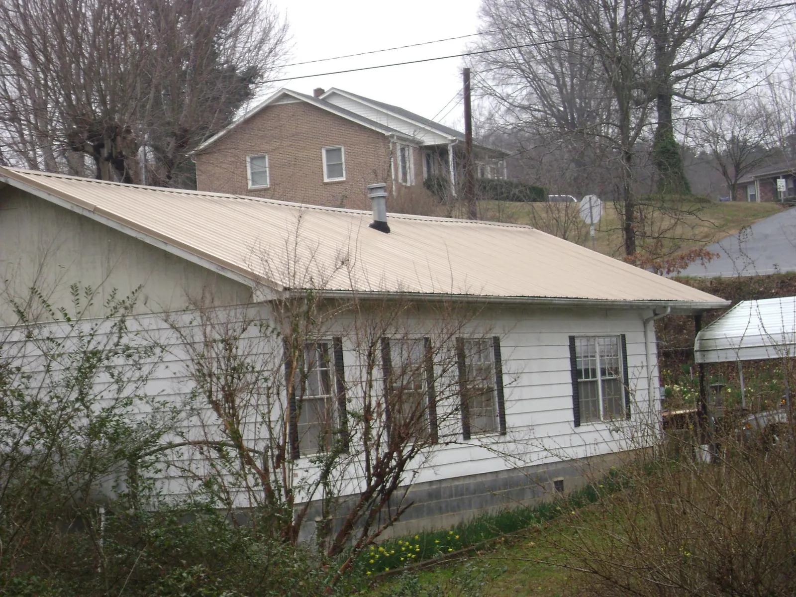 Tan metal roof on a white sided house set into a hillside — Commercial Roofing by Roofing Brothers in Thiells